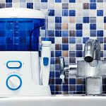 Closeup of a water flosser on a white sink against a blue mosaic backsplash