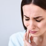 Brunette woman touches her cheek due to braces pain