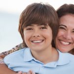 Brunette boy with braces smiles on the beach with his brunette mother