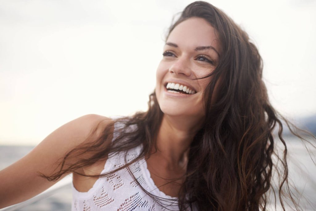 Brunette woman with straight teeth smiles after getting her braces off because of all the benefits of straight teeth