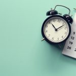 Aerial view of an alarm clock next to a calendar on an aqua green background