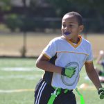 Young Black boy playing flat football while wearing an athletic mouthguard to protect his smile.
